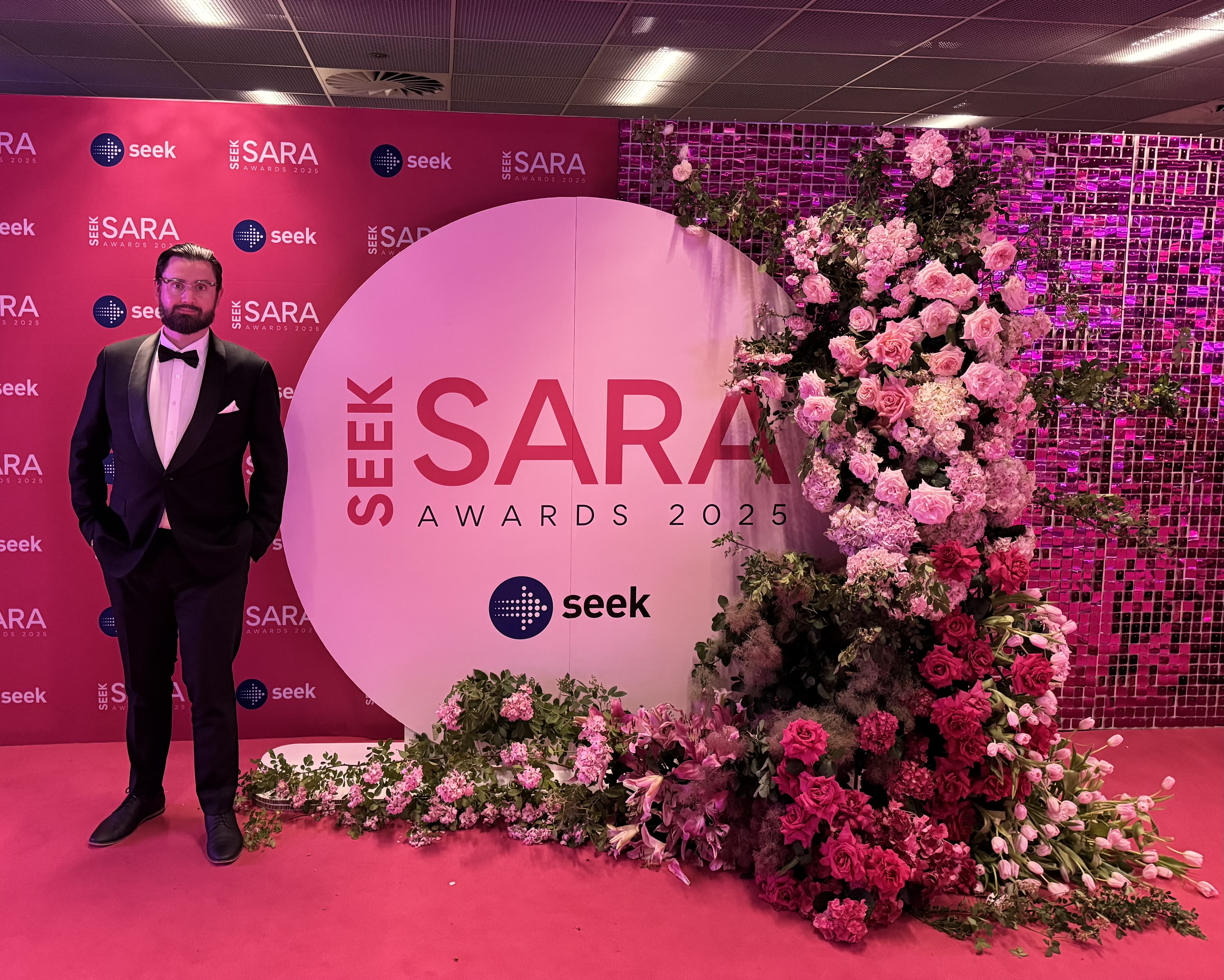 Martyn J Hill in formal attire beside the SEEK SARA Awards 2025 backdrop.